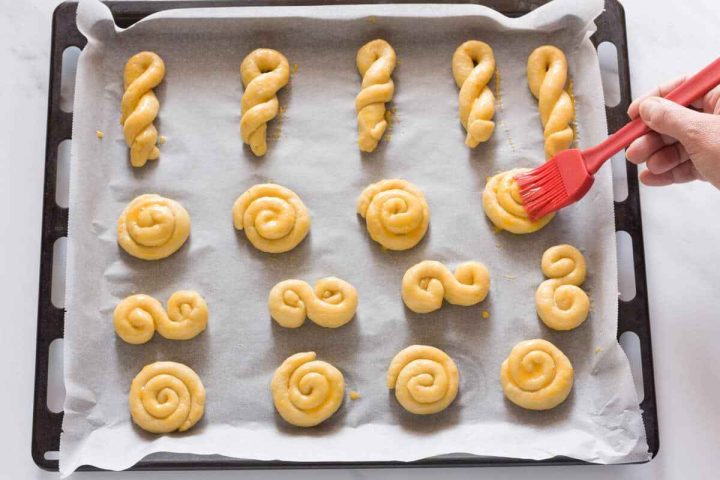Traditional koulourakia cookie shapes brushed with egg wash before baking.