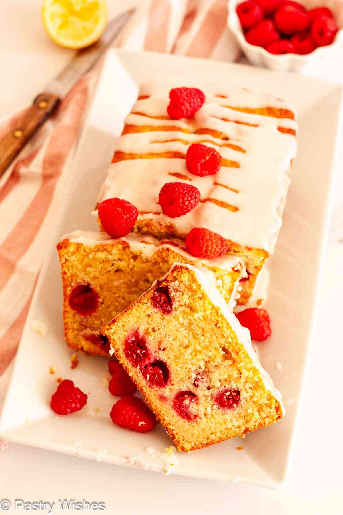 iced lemon raspberry loaf cake on a white platter with fresh raspberries.