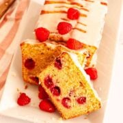 A close up of sliced raspberry loaf cake on a white platter with fresh raspberries.