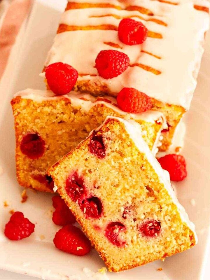 A close up of sliced raspberry loaf cake on a white platter with fresh raspberries.