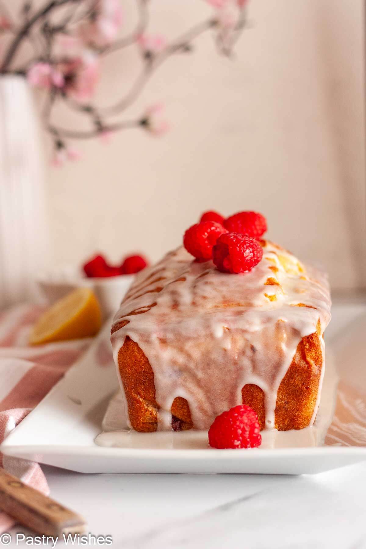 A lemon raspberry loaf cake on a white platter topped with glaze and fresh raspberries.
