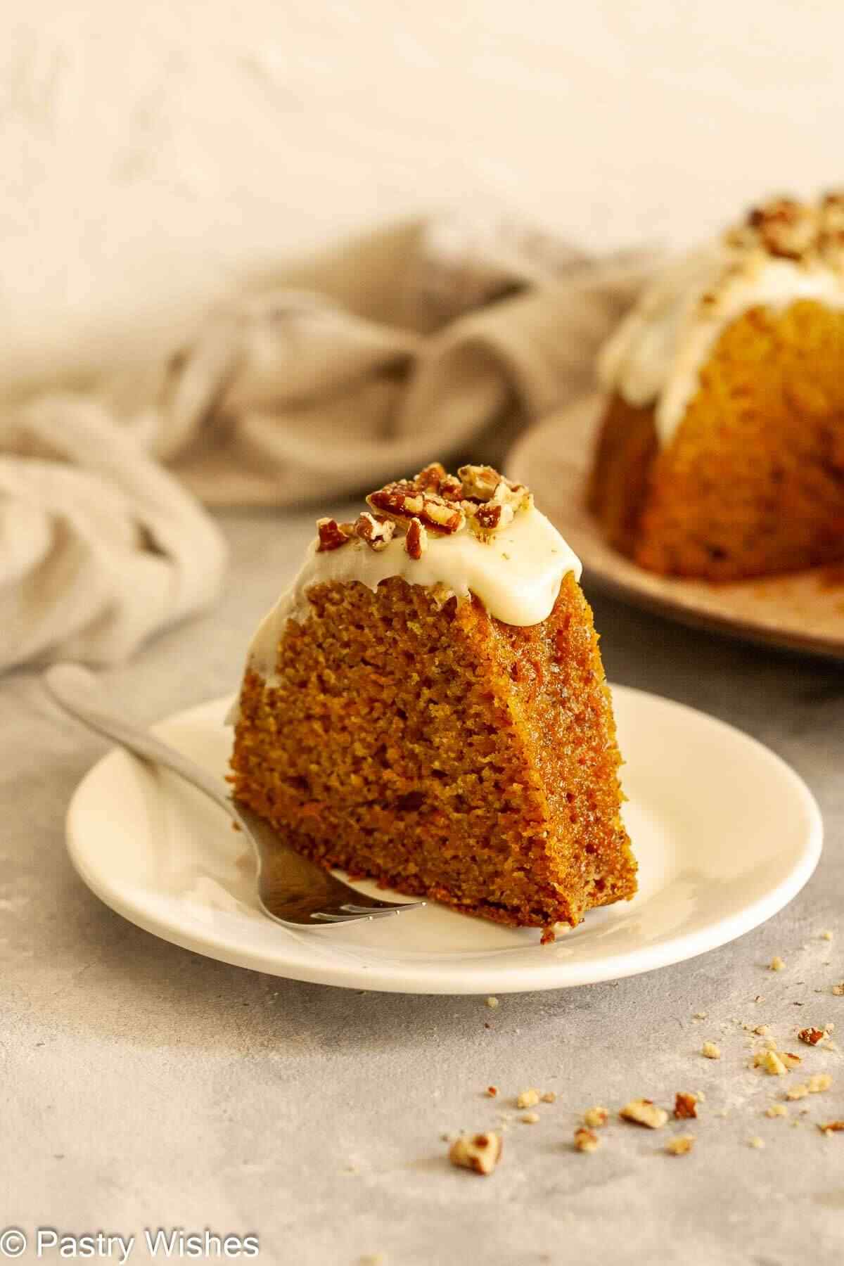 A slice of carrot Bundt cake with cream cheese glaze on a white plate with a fork.