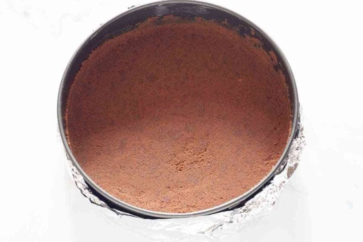 Pressing chocolate cookie crust into springform pan lined with parchment.