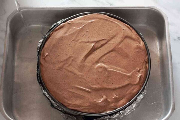 Cheesecake in springform pan placed in water bath.