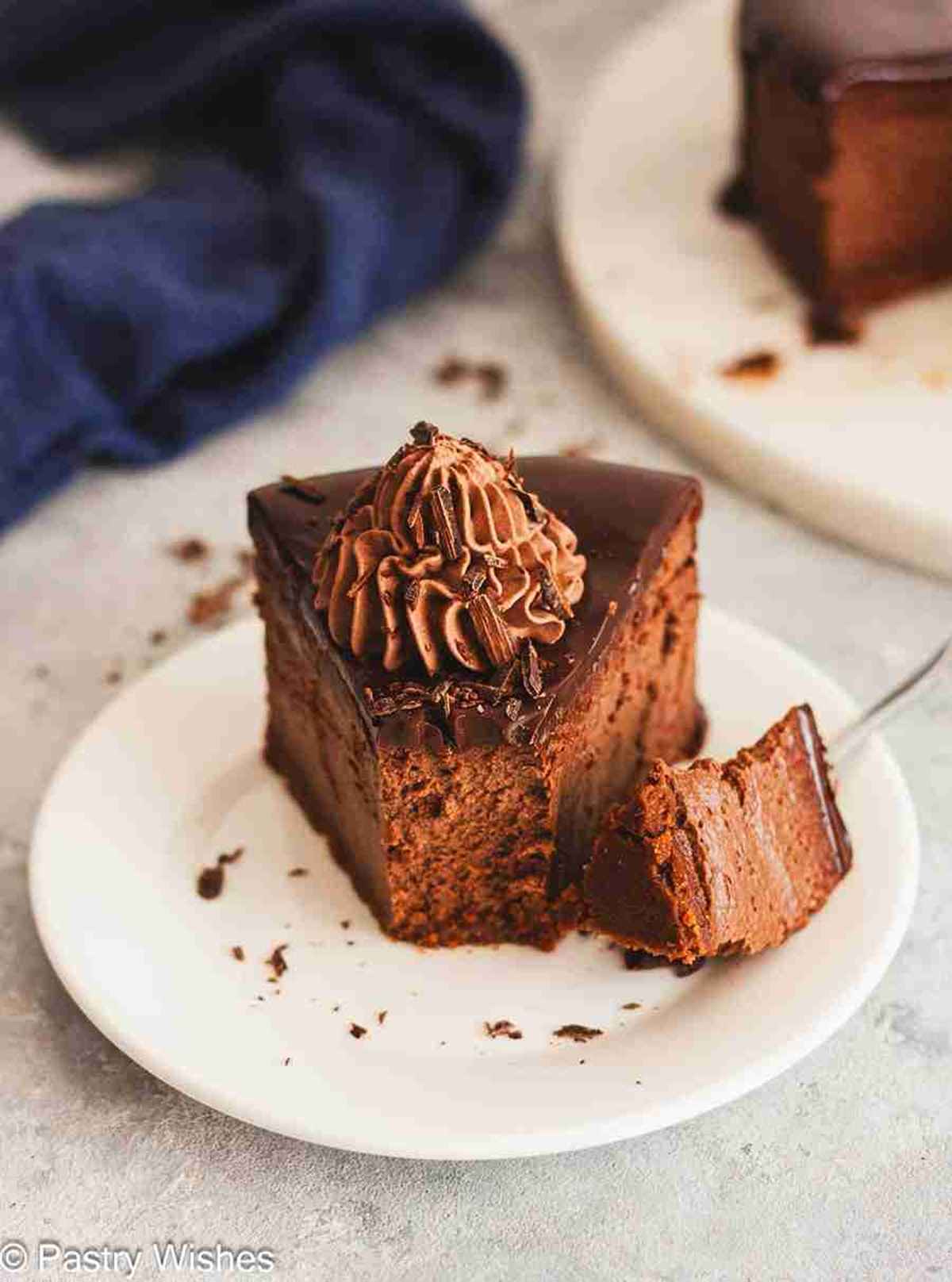 Slice of chocolate ganache cheesecake topped with whipped cream on a plate with a bite taken out.