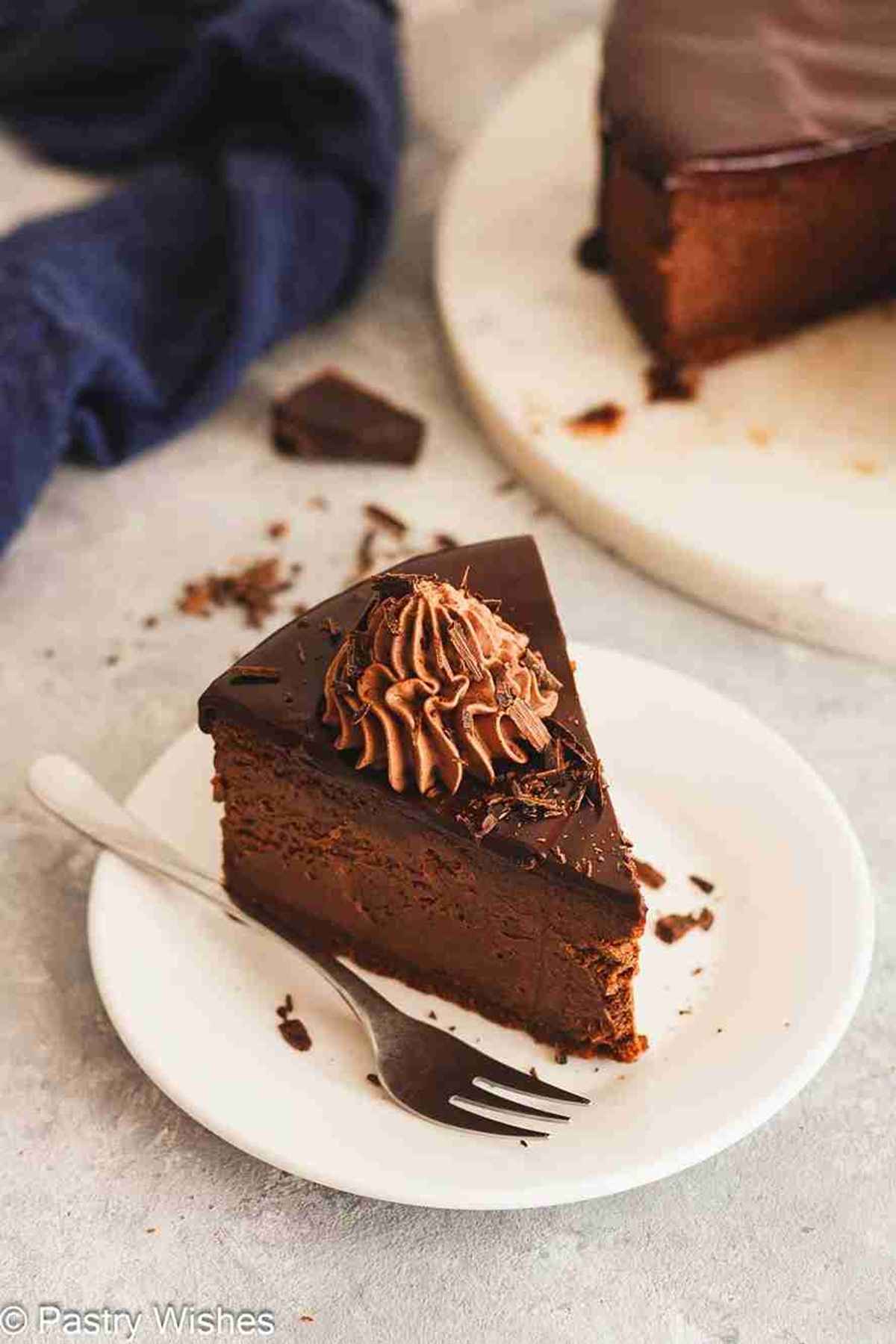 Slice of chocolate ganache cheesecake topped with whipped cream on a plate with a fork.