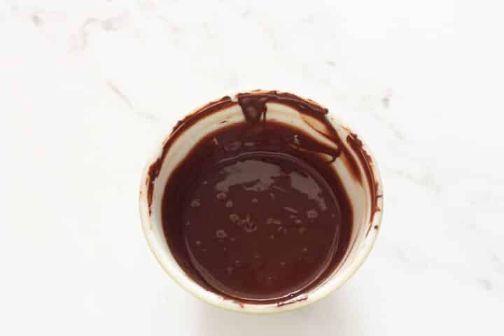 Melted semi-sweet chocolate in a bowl for chocolate ganache cheesecake.