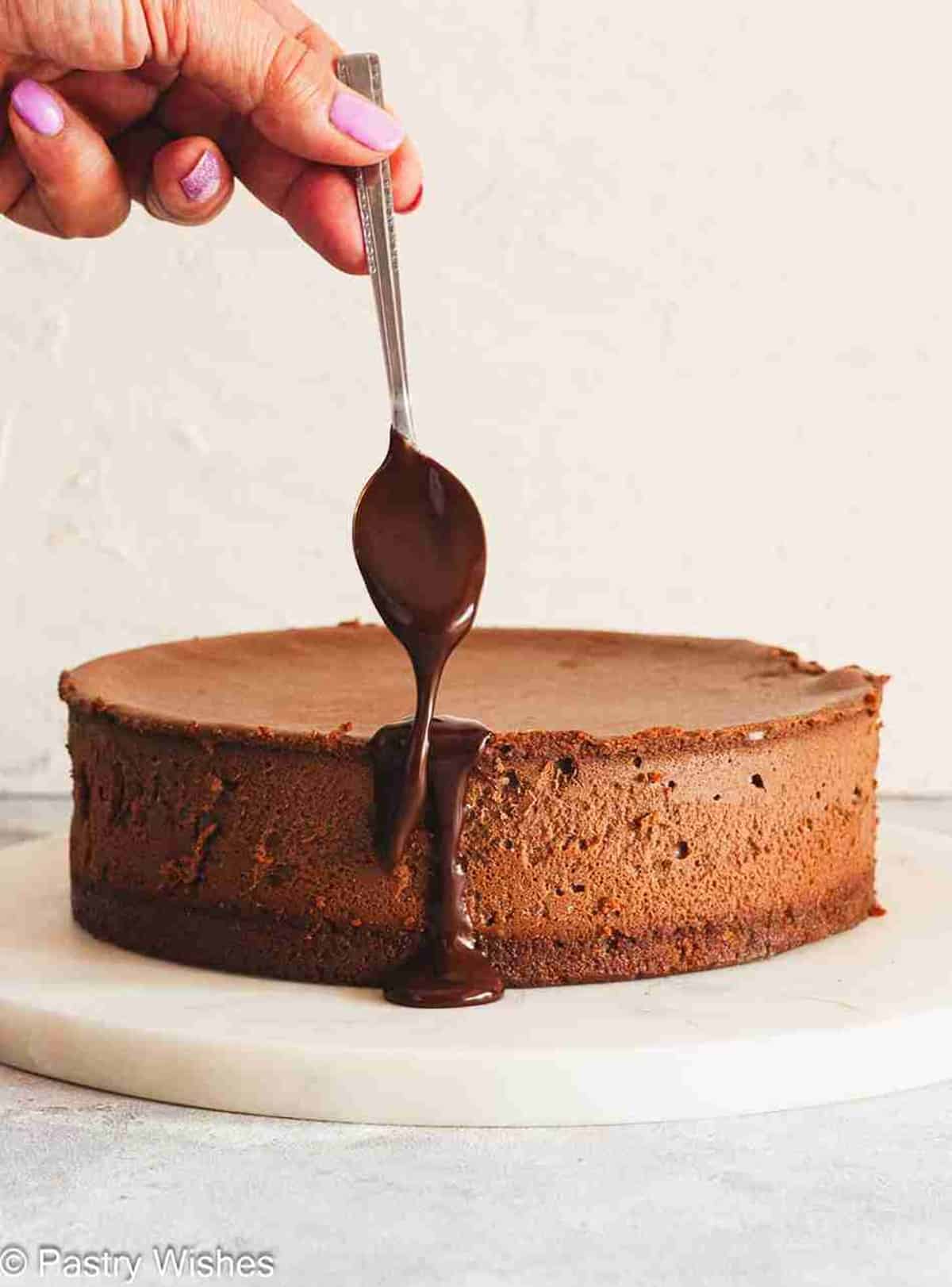 Pouring chocolate ganache over baked chocolate cheesecake.