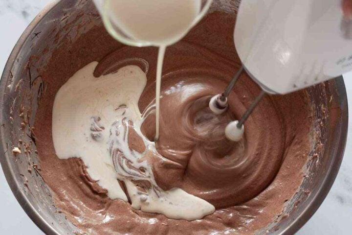 Heavy cream poured into chocolate cheesecake batter.