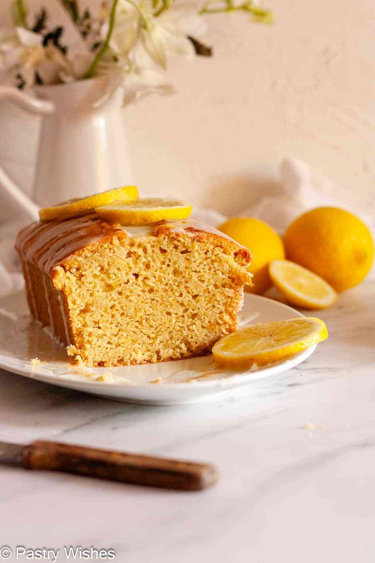 Close-up of moist eggless lemon loaf cake with lemon glaze and lemon slices on a plate.