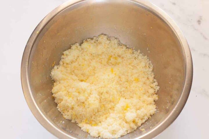 Sugar mixed with fresh lemon zest in a metal bowl for eggless lemon cake.
