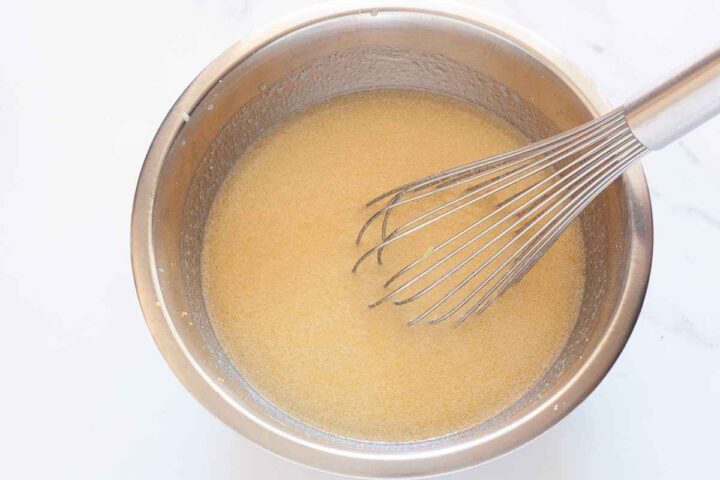 Wet ingredients whisked together with lemon sugar in a bowl for eggless lemon cake batter.