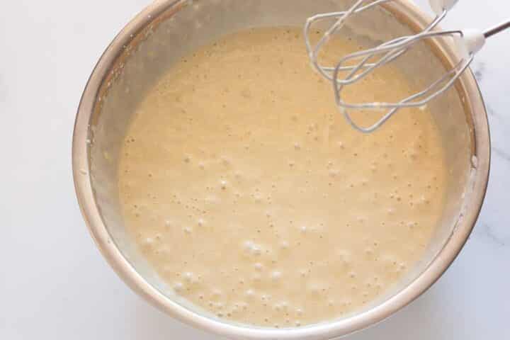 Combined eggless lemon cake batter in a metal bowl with a hand mixer.