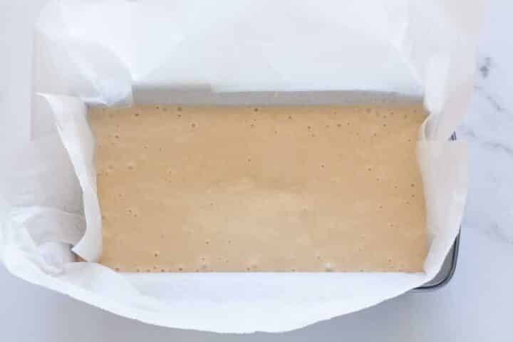 Eggless lemon cake batter poured into a parchment-lined loaf pan before baking.