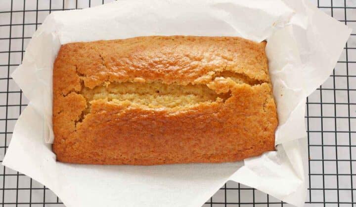 Freshly baked eggless lemon loaf cake cooling in the pan on a wire rack.
