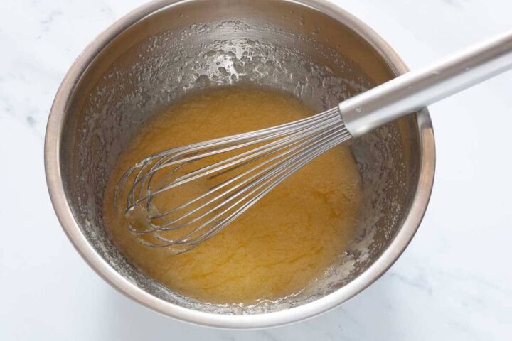 Whisking melted butter and sugar together in a metal bowl for Greek yogurt blueberry muffins.