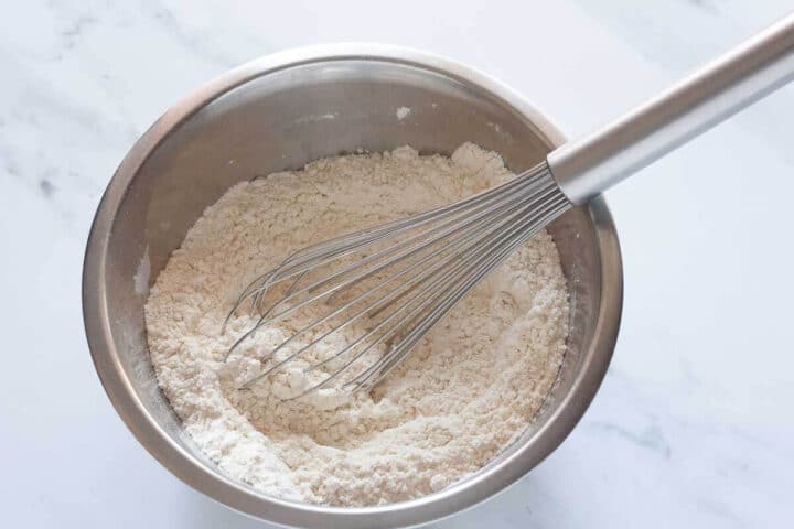 Dry ingredients for Greek yogurt blueberry muffins in a mixing bowl with a whisk.