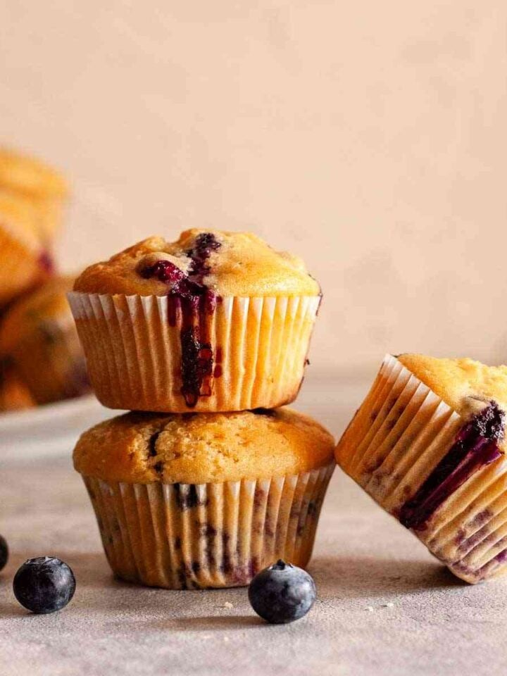 Dairy-free blueberry muffins with golden tops, juicy blueberries, and fresh blueberries on the side.