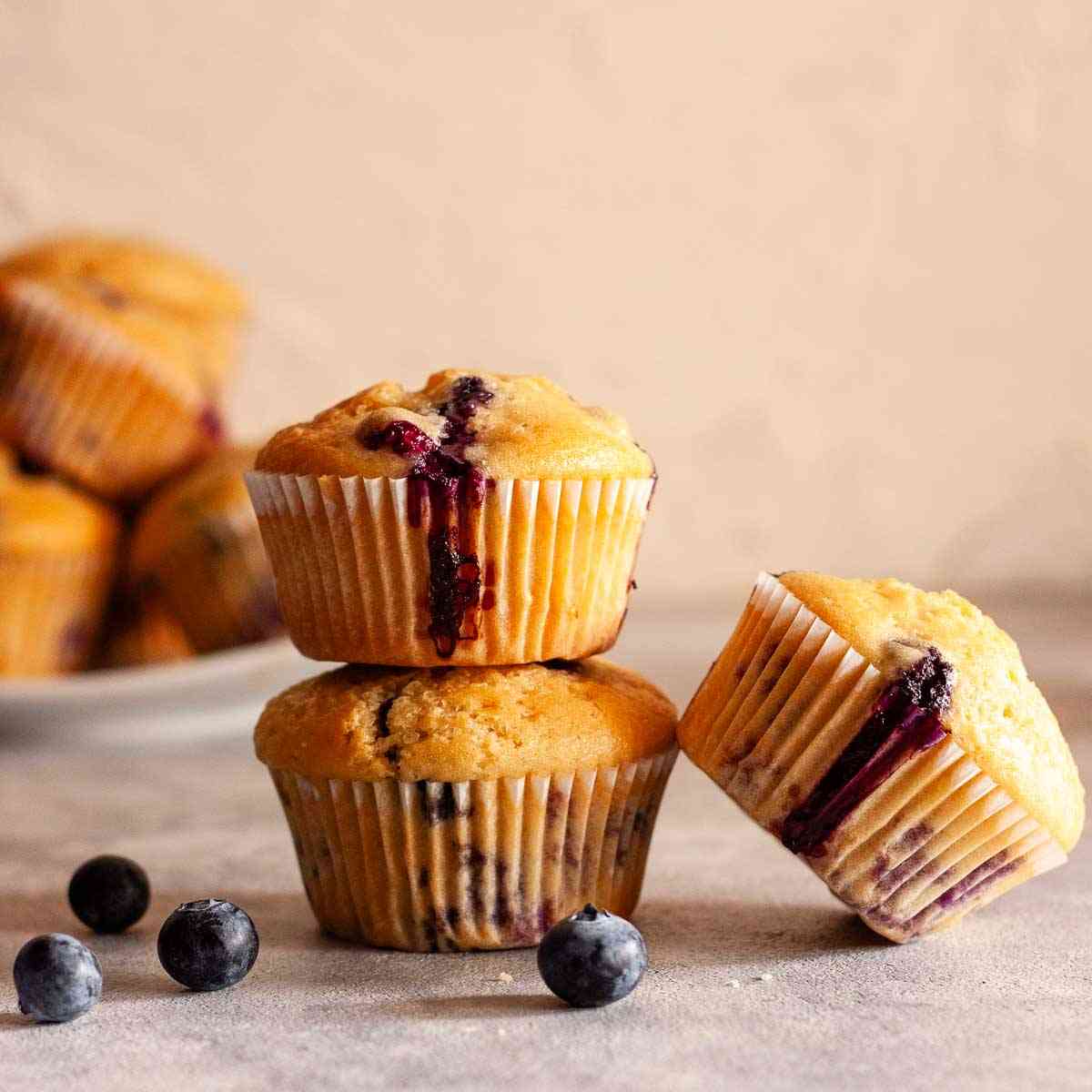 Dairy-free blueberry muffins with golden tops, juicy blueberries, and fresh blueberries on the side.