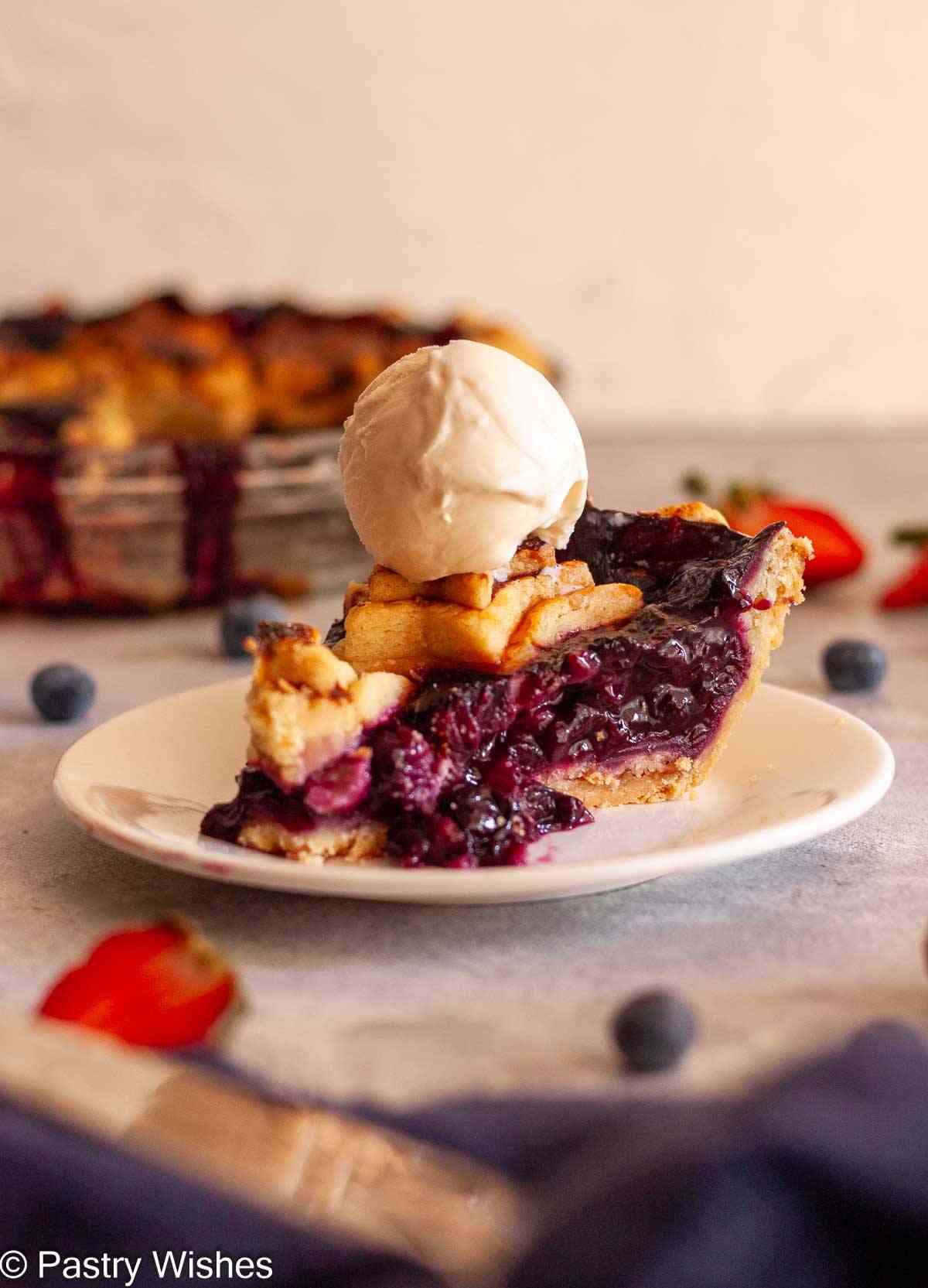Strawberry blueberry pie slice topped with vanilla ice cream.