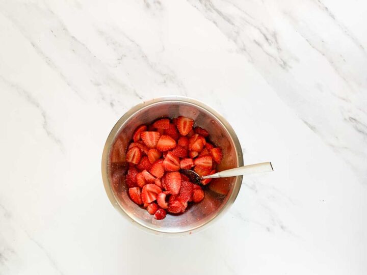 Sliced strawberries tossed with sugar and lemon juice in a bowl.