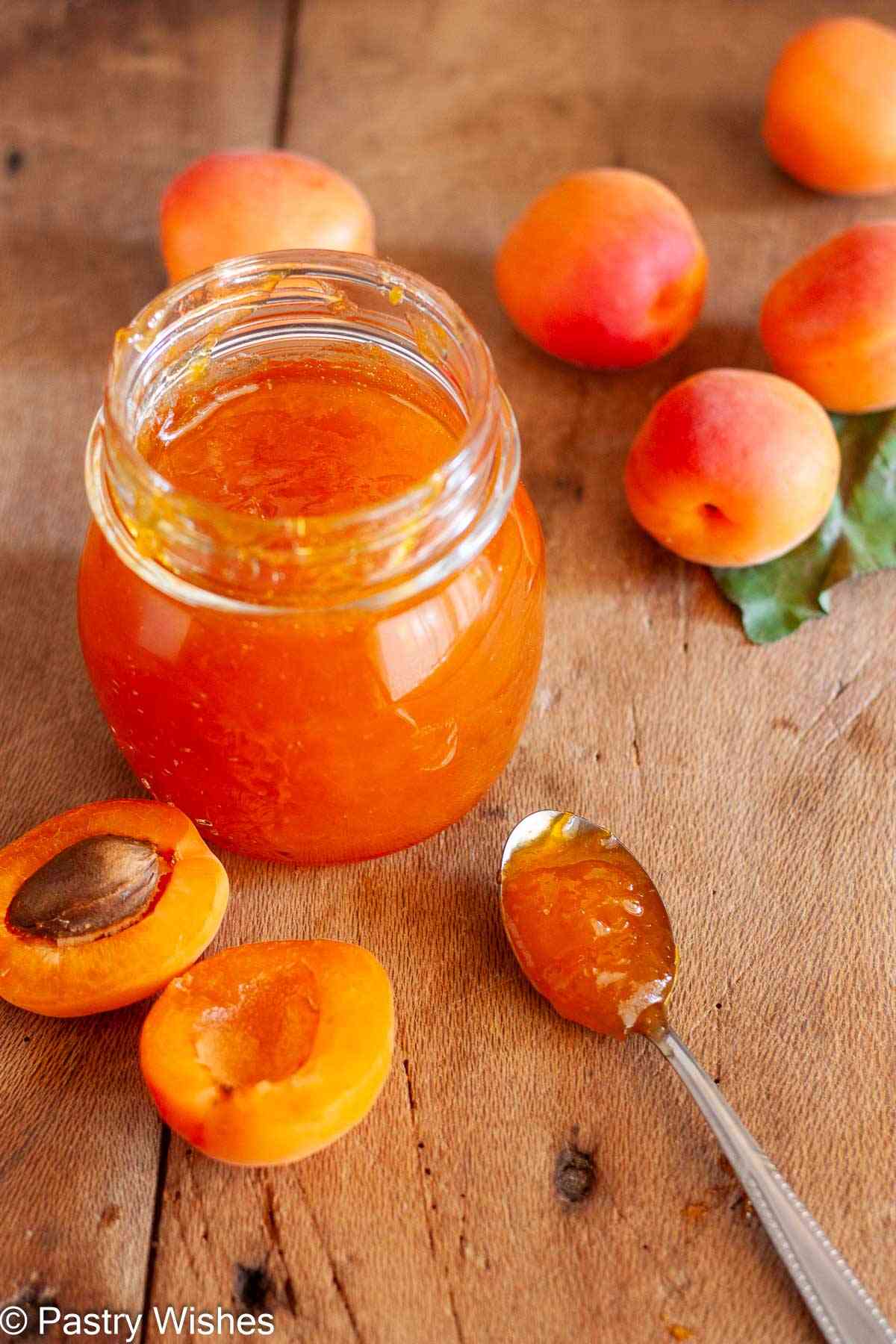 Close-up of homemade apricot jam in a glass jar with a spoon and fresh apricot halves.