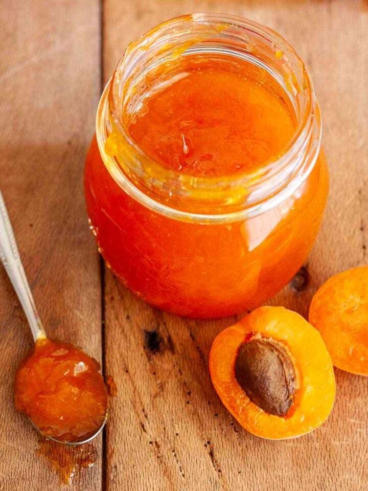 Homemade apricot jam without pectin in a glass jar with fresh apricots and a spoonful of jam.