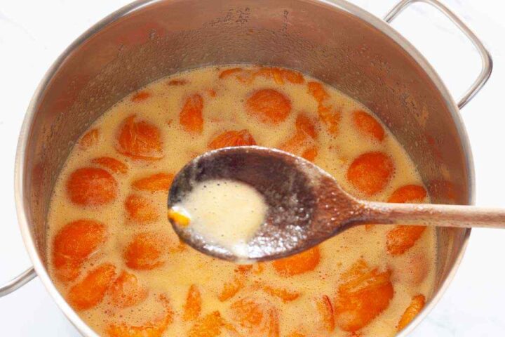 Step 3: Skimming foam from simmering apricot jam with a wooden spoon.