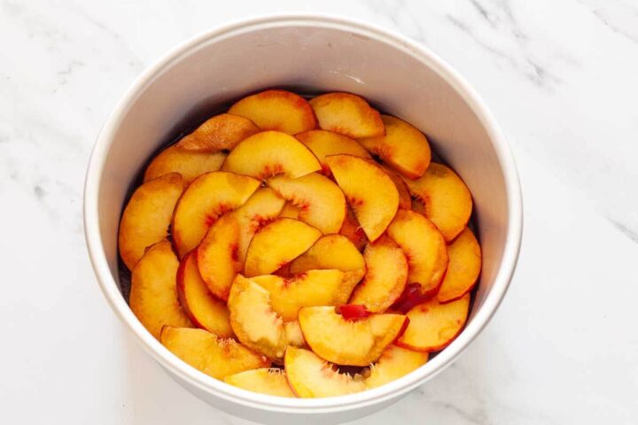 Sliced peaches arranged in overlapping circles over bourbon caramel in a round cake pan.