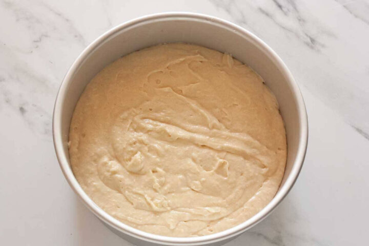 Cake batter spread evenly over the arranged peaches in a round cake pan.