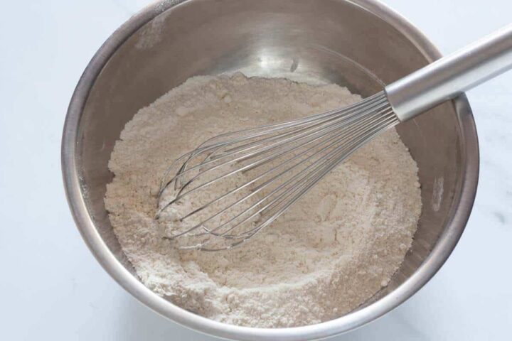 All-purpose flour, almond flour, baking powder, and salt being whisked together in a bowl.