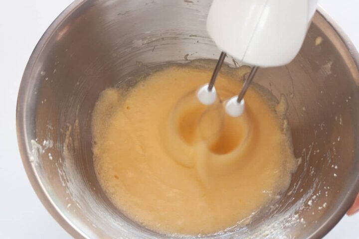 Butter, sugar, eggs, and vanilla being beaten together with a hand mixer.