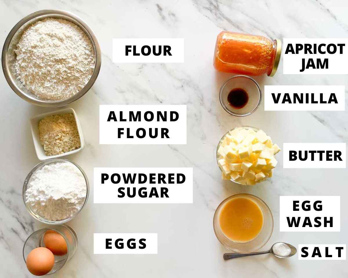 Labeled ingredients for Greek pasta flora, including flour, butter, powdered sugar, almond flour, eggs, vanilla, salt, apricot jam, and egg wash.