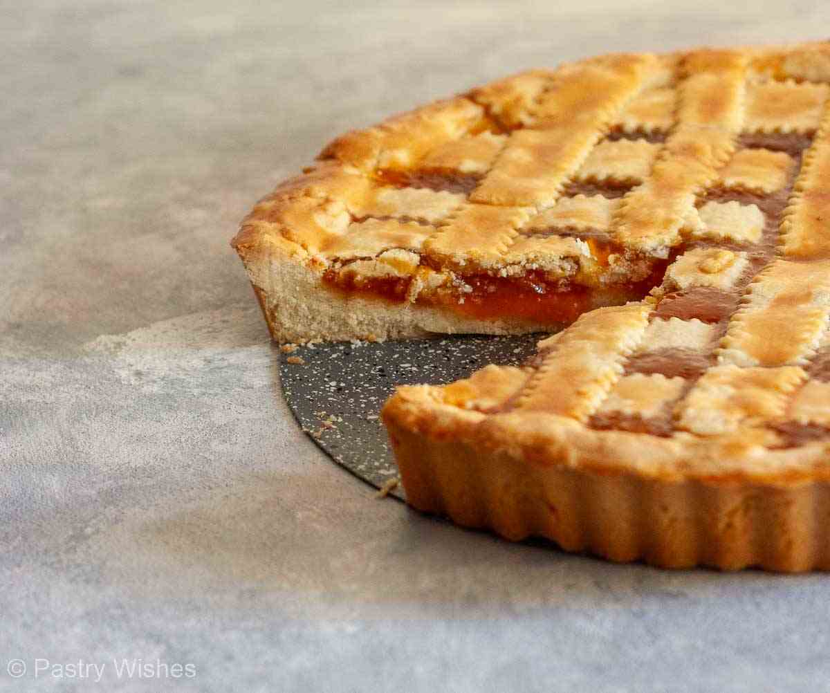Greek pasta flora tart in a pan with a slice removed showing the apricot jam layer.