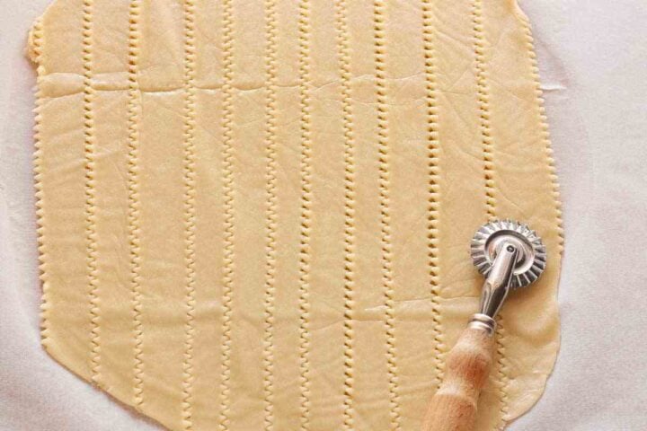 Pasta flora topping dough cut into strips with a fluted pastry wheel.