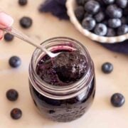 Spoonful of homemade blueberry jam without pectin over an open jar with fresh blueberries in the background.