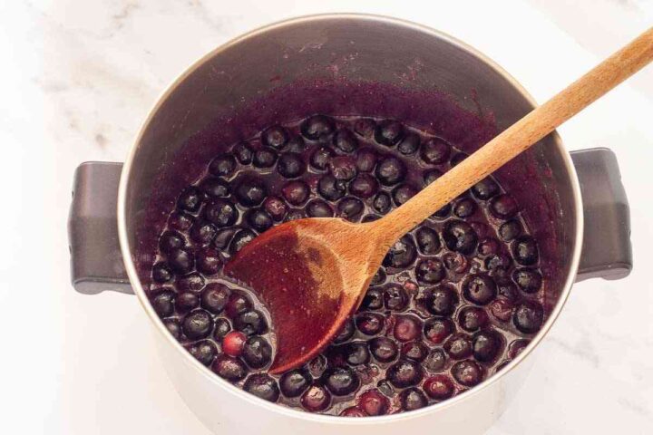 Blueberries cooking in their juices with a wooden spoon in the saucepan.