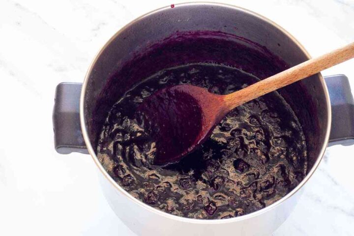 Blueberry jam cooked until thick and glossy in a saucepan.