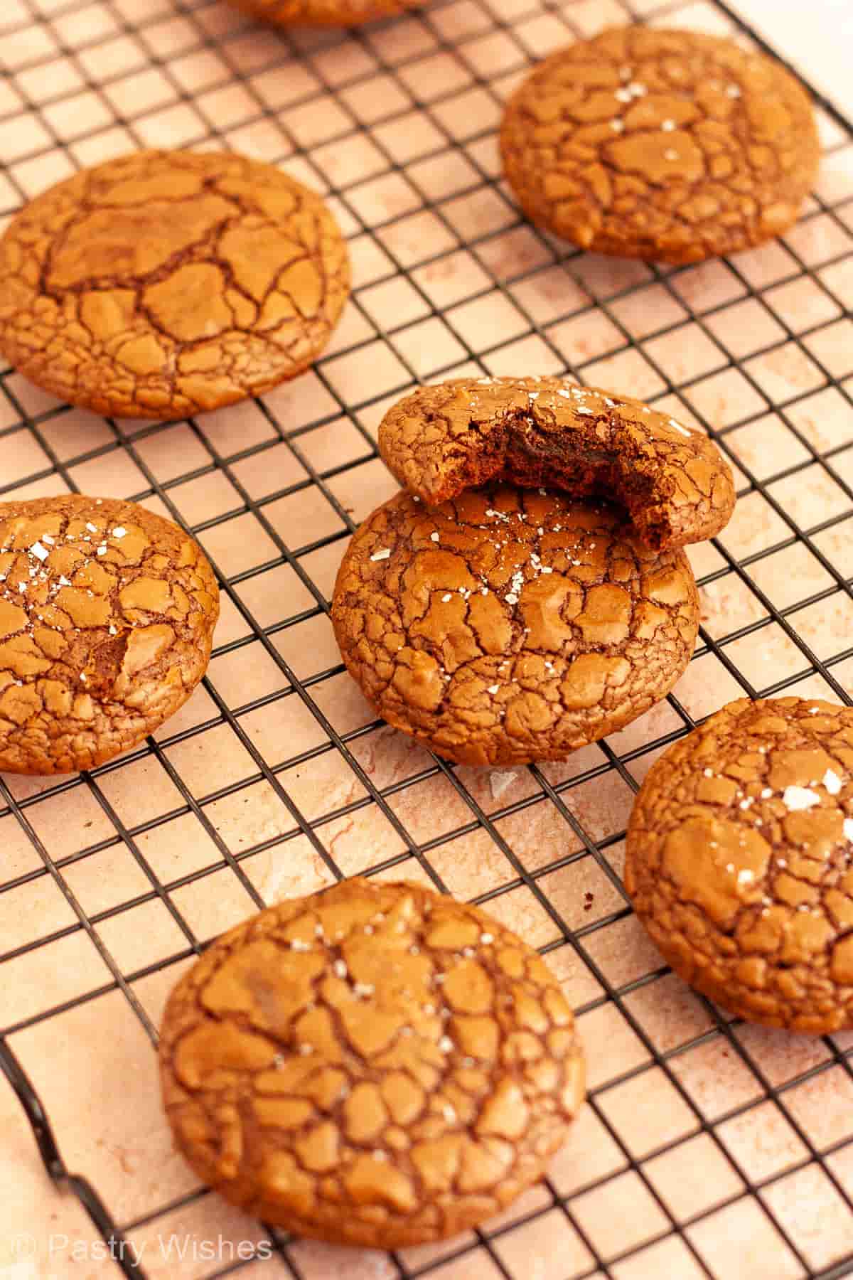 Brownie crinkle cookies cooling on a wire rack with one bitten cookie showing the fudgy center.