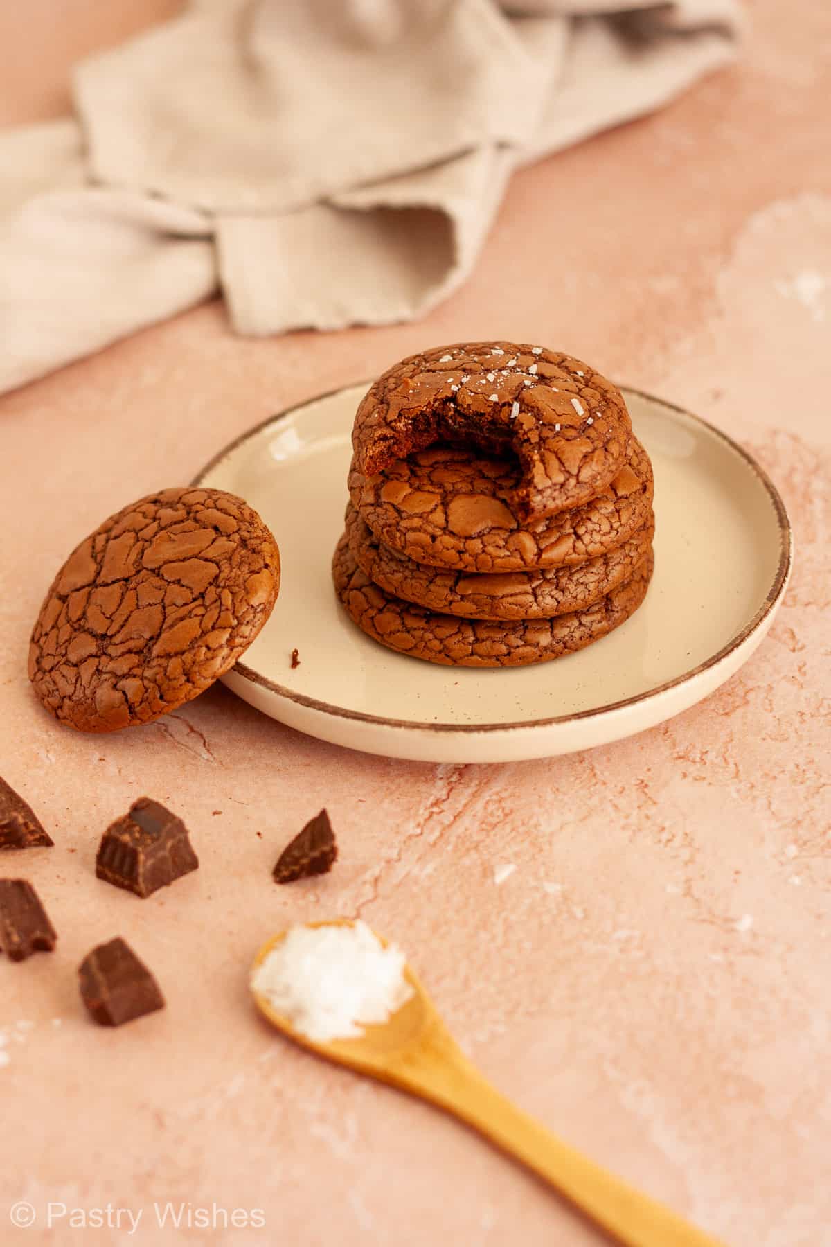 Stacked brownie crinkle cookies with a bitten cookie showing the soft fudgy center.