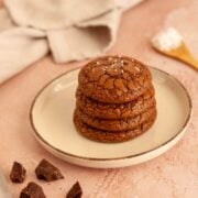 Stack of four brownie crinkle cookies with flaky sea salt on a plate.