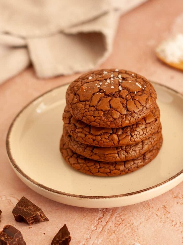 Stack of four brownie crinkle cookies with flaky sea salt on a plate.