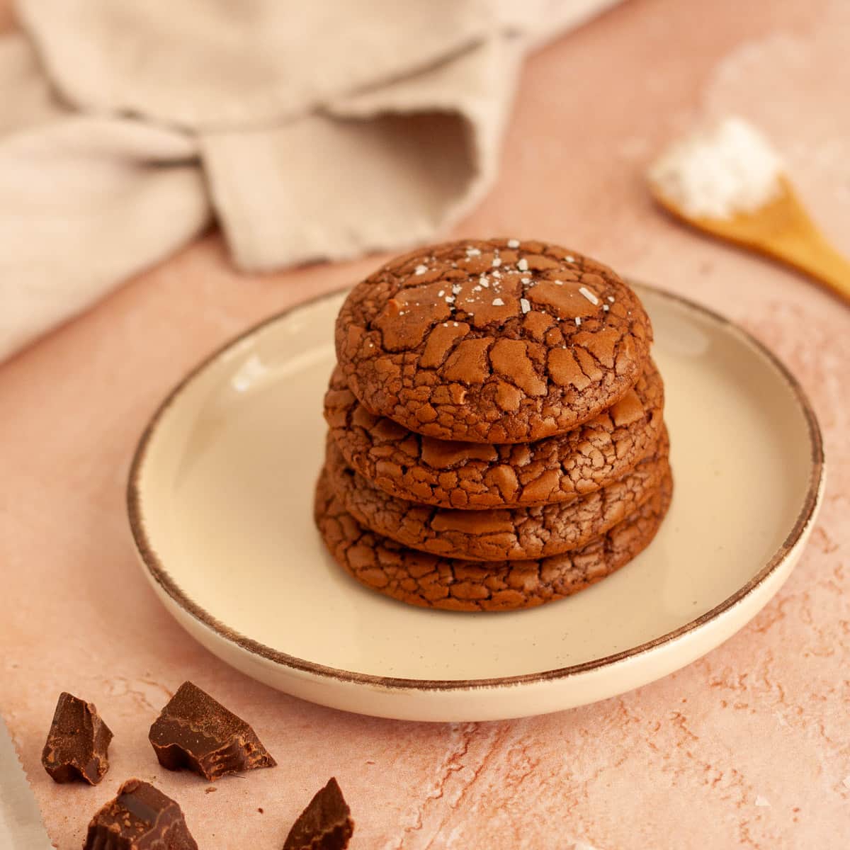 Stack of four brownie crinkle cookies with flaky sea salt on a plate.
