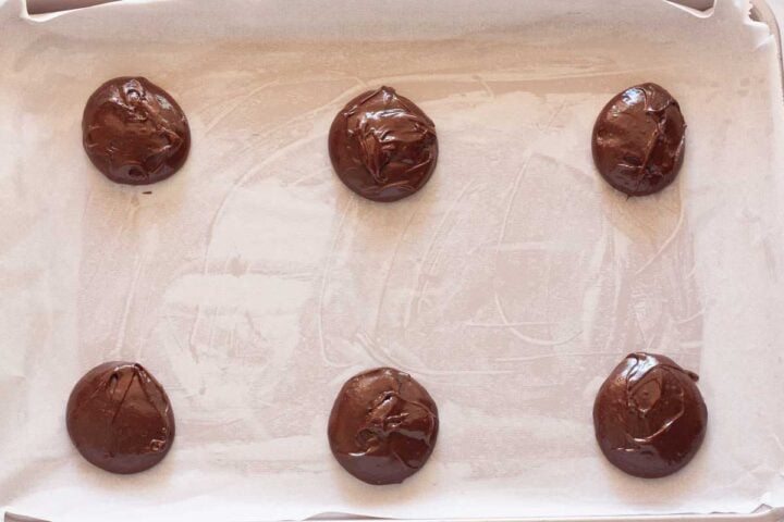 Scoops of brownie cookie batter spaced apart on a parchment-lined baking sheet.