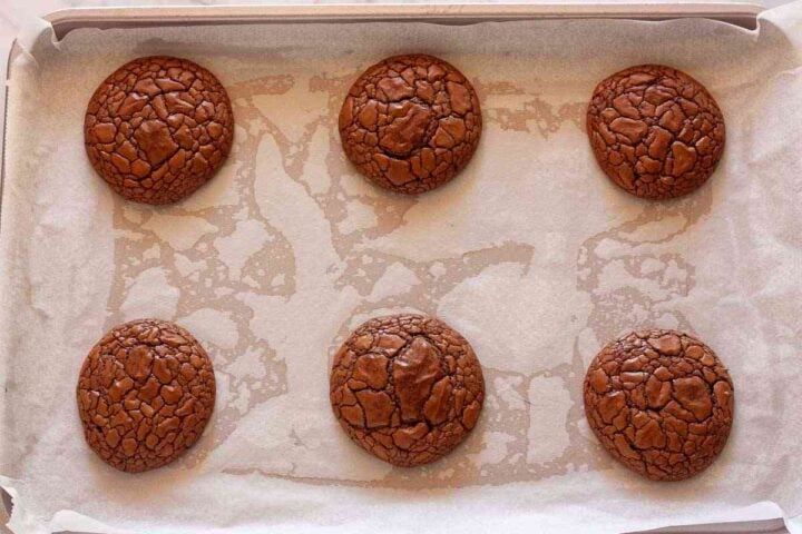 Freshly baked brownie crinkle cookies with shiny cracked tops on a baking sheet.