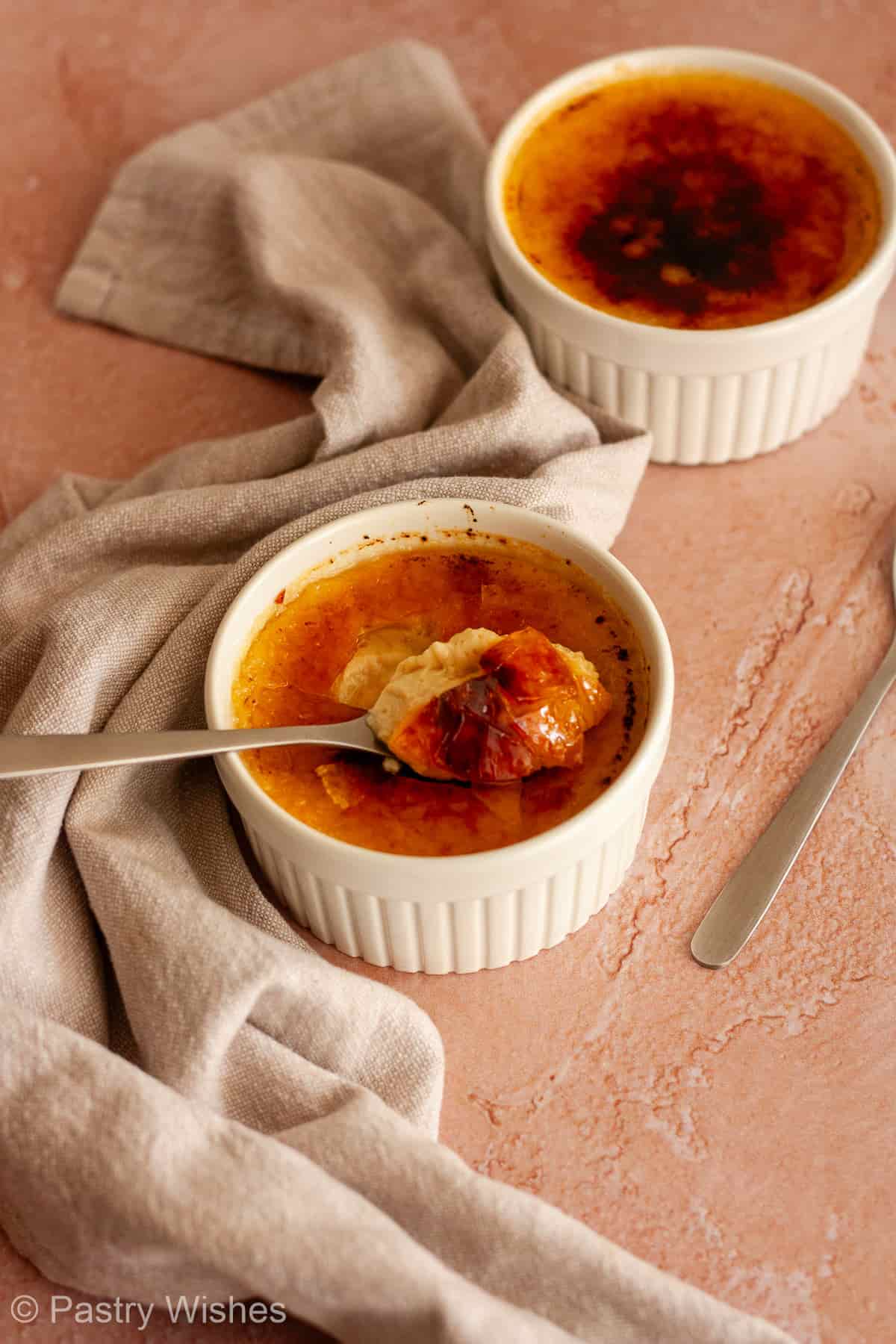 Spoonful of vanilla custard and caramelized sugar resting over a crème brûlée ramekin.