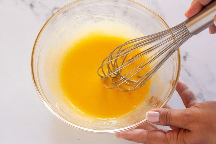 Whisking egg yolks and sugar together in a glass mixing bowl.