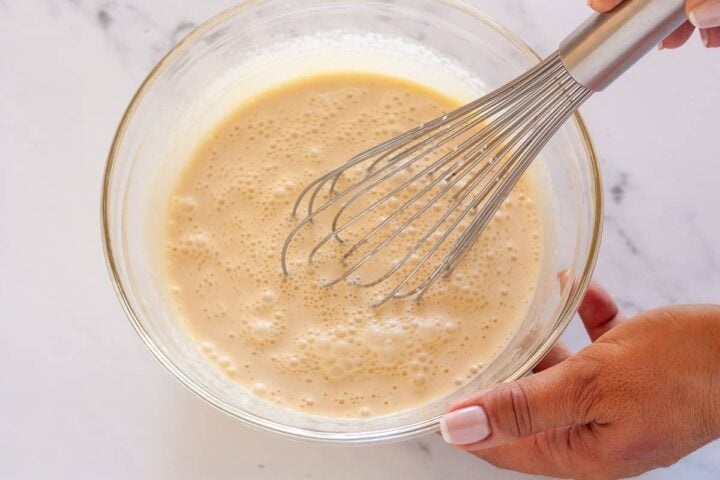 Whisking the cream, milk, and vanilla into the egg yolk mixture.