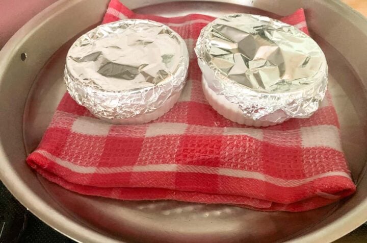 Two foil-covered ramekins in a stovetop water bath.